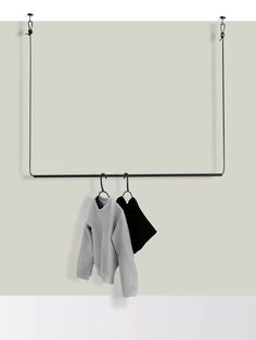 two sweaters hanging from hooks on a white and gray wall next to a coat rack