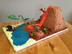 a dinosaur themed birthday cake on a wooden table with trees and rocks in the background