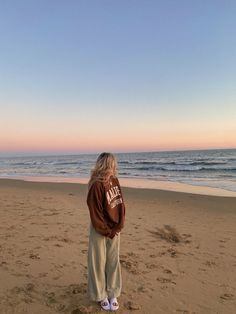 a woman standing on top of a sandy beach next to the ocean under a blue sky