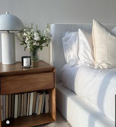 a bed with white sheets and pillows next to a wooden night stand filled with books