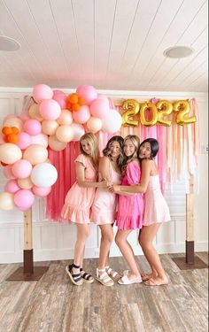 three girls standing in front of a balloon arch with pink and orange balloons on it