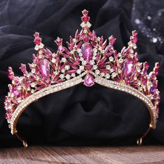 a tiara with pink and white stones sits on a wooden table next to a black cloth