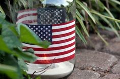 a glass jar with an american flag painted on it sitting in front of some plants