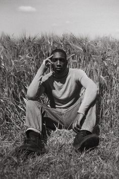 a man sitting in the middle of a field talking on a cell phone