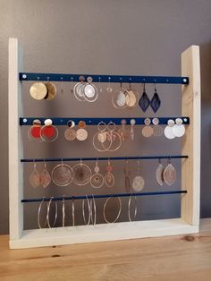 a wooden frame holds several pairs of earrings and earring hooks on a wall mounted jewelry rack