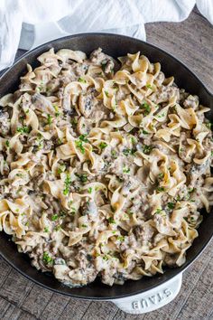 a skillet filled with pasta and mushrooms on top of a wooden table next to napkins