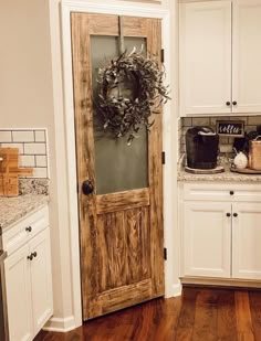 a wooden door with a wreath on it in a kitchen next to white cupboards