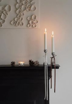 two candles are lit in front of a fireplace with decorations on the wall behind it