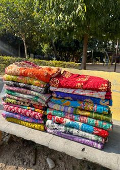 a pile of colorful cloths sitting on top of a cement bench next to trees