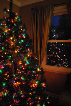 a brightly lit christmas tree in front of a window