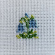 a cross stitch pattern with blue flowers and green leaves on white fabric, in the shape of a ship