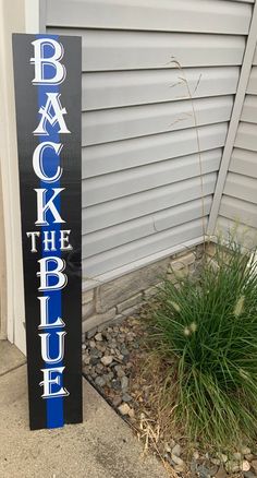 a black and blue sign that says back the blue next to some grass in front of a house