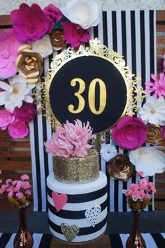 a black and white striped cake with pink flowers on the top is decorated with gold numbers