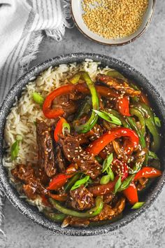 a bowl filled with beef and peppers on top of rice next to a plate of sesame seeds