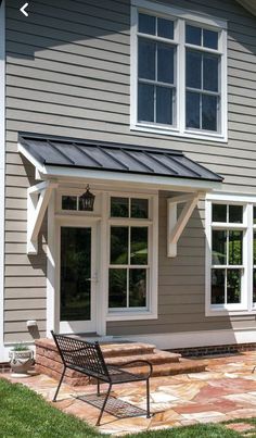 a gray house with white windows and a black bench in front of the porch area