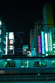 a train traveling through a city at night with tall buildings in the backgroud