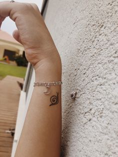 a woman's arm with a small tattoo on it and a snail charm attached to the wrist