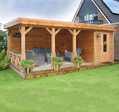 a large wooden covered patio with chairs and plants on the grass in front of it