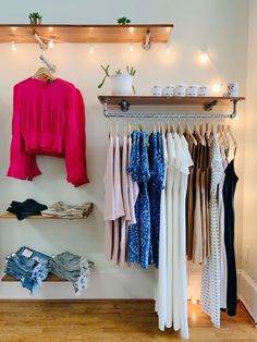 clothes are hanging on the rack in front of a wall mounted shelf with lights above it