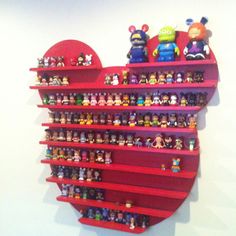 a red shelf filled with lots of toy figurines next to a white wall