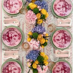 the table is set with pink and yellow plates, silverware, and floral centerpieces