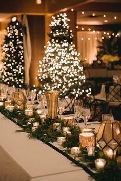 a long table with candles and christmas trees in the background at a wedding or event