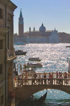 people are standing on a bridge over the water in front of some buildings and boats