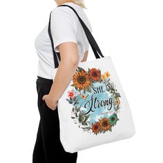 a woman carrying a white tote bag with sunflowers and the words she is strong