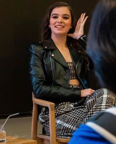 a woman sitting in a chair with her hand on her head while talking to another person