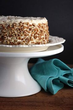 a cake with white frosting and pecans on top sitting on a plate next to a blue napkin