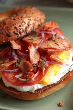 an open face sandwich with bacon, eggs and tomatoes on a bagel bun sitting on a green plate