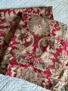 two pieces of red and gold brocaded fabric on a bed with white sheets