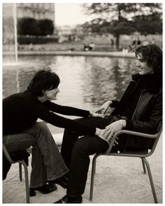 black and white photograph of two people sitting on chairs facing each other with water in the background