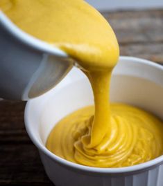 a person pouring yellow sauce into a white bowl