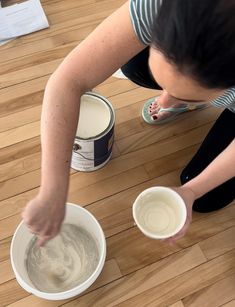 a woman sitting on the floor with two cups in front of her and one holding a paintbrush