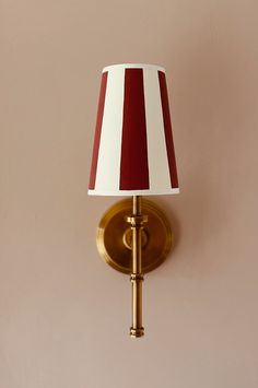 a red and white striped lamp on a wall next to a pink wall with a gold frame