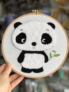 a person holding up a small embroidered panda bear