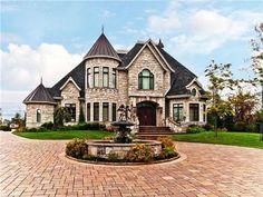 a large brick driveway with a fountain in front of a house on a sunny day