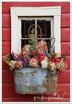 an old metal bucket filled with flowers next to a red building and a white window