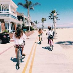 three people riding bikes on the sidewalk near palm trees