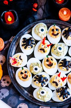 devil's eggs decorated with googly eyes and black noses are on a platter surrounded by halloween candles