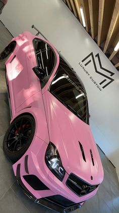 a pink sports car is parked in front of a wall with a logo on it