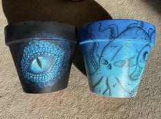 two vases sitting on the ground with designs painted on them, one has an eye in it