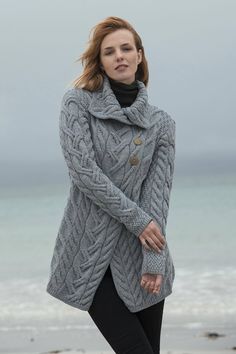 a woman standing on the beach wearing a gray coat