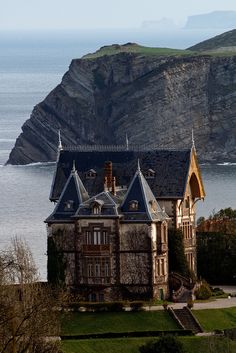 a black and white photo of an old house by the ocean with mountains in the background