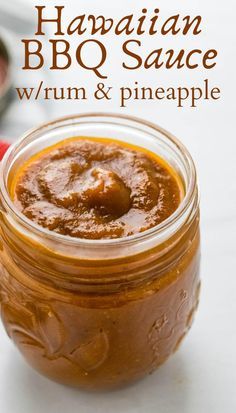 a jar filled with bbq sauce sitting on top of a white table next to a spoon