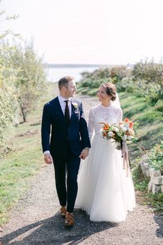 a bride and groom walking down a path holding hands