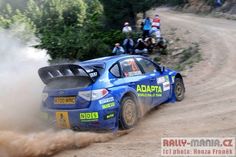 a blue car driving down a dirt road with people watching from the side of it