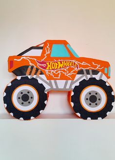 an orange monster truck with black wheels on a white shelf next to a wall mounted clock