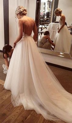 a woman in a white wedding dress looking at herself in the mirror while another person is fixing her dress